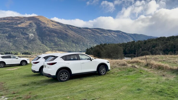 La cámara realiza una panorámica sobre varios todoterrenos blancos aparcados en el pintoresco valle de Queenstown, a plena luz del día, con exuberantes montañas visibles