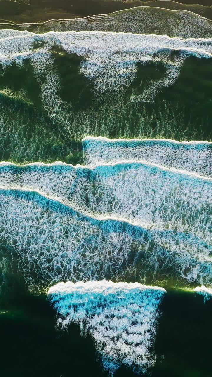 Amazing beautiful waves moving the sandy beach of Morro Bay, California, USA. White foamy tide slowly moving to the shore. Bird's eye view. Vertical video