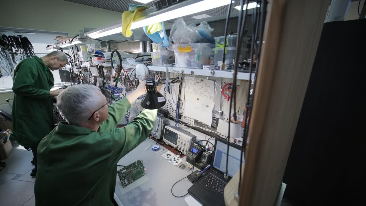 tienda de reparación de equipos electrónicos. el técnico ingeniero soldada la placa de circuitos impresos de un dispositivo electrónico bajo un microscopio.