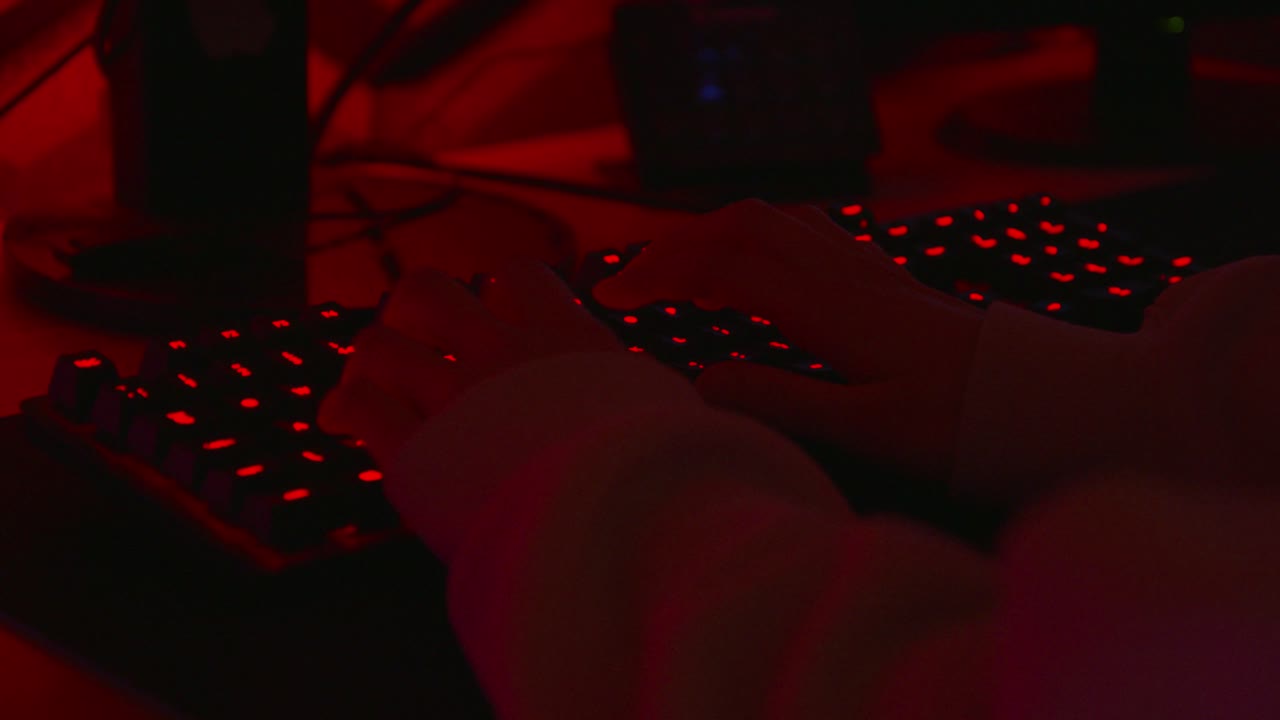 анонимный хакер в темной красной комнате печатает на красной клавиатуре