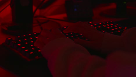 anonymous hacker in a dark red room typing on red keyboard