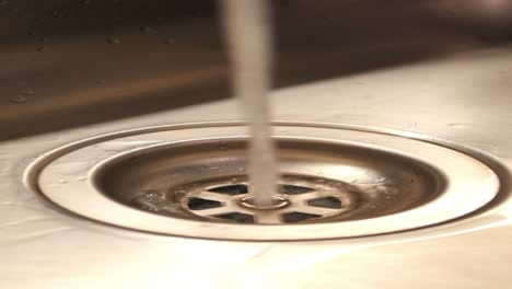 agua que entra en un desagüe de fregadero de acero inoxidable