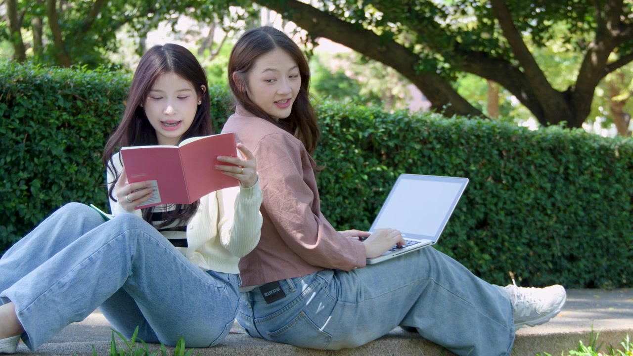 亞洲學生在校園窗台上背對背坐著，使用手提電腦和書本。
