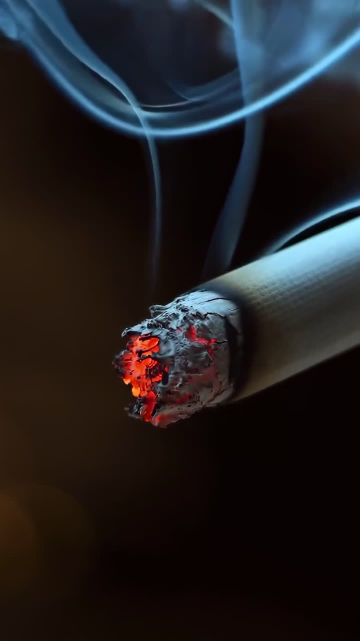 Primer plano de un cigarrillo encendido con humo ascendente y brasa incandescente.