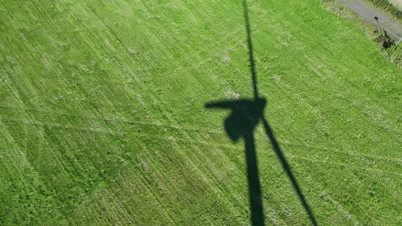 Aerial: shade of wind turbine in the grass during the day with sunshine, outdoor, establishing drone shot