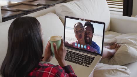 mujer afroamericana sosteniendo una taza de café haciendo una videollamada en una computadora portátil sentada en el sofá en casa