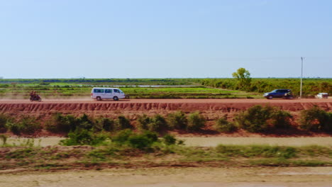 local traffic traveling along a red mud dike roadway near kampong cambodia, aerial track