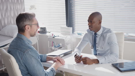 mature male patient sitting at desk having consultation with doctor in office