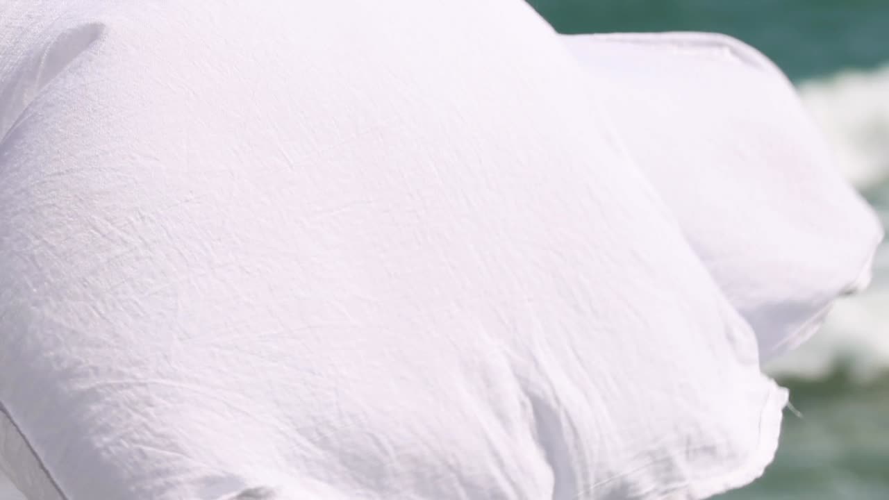 Close-up of white fabric gently flowing with ocean waves in the background.