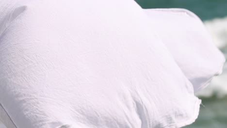 close-up of white fabric gently flowing with ocean waves in the background.