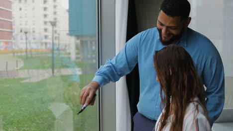 hombre barbudo alto y mujer joven dibujando gráficos en la ventana.