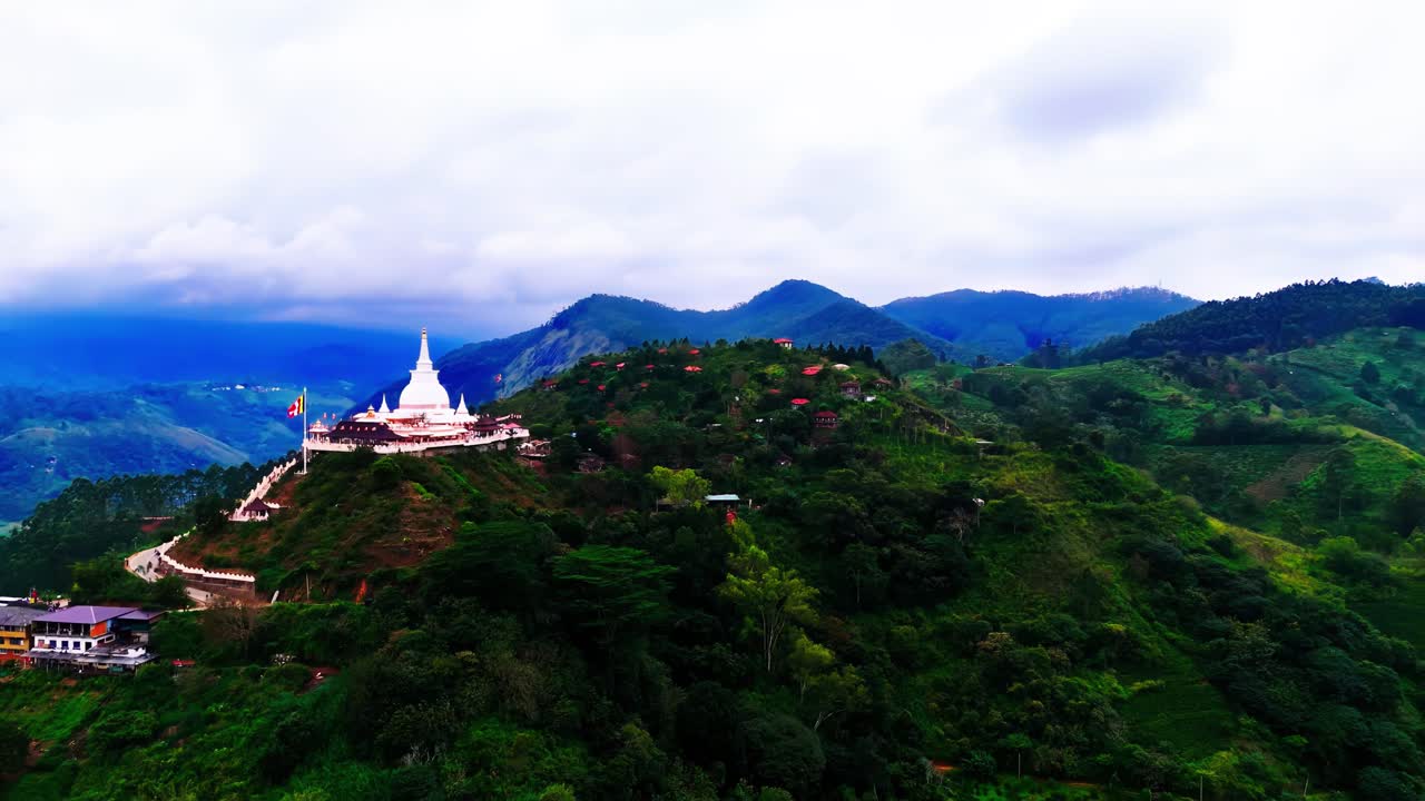 A brilliant white Buddhist temple stands atop a Sri Lankan hill, surrounded by lush green mountains, winding paths, and misty skies, offering a serene cultural and spiritual landscape.