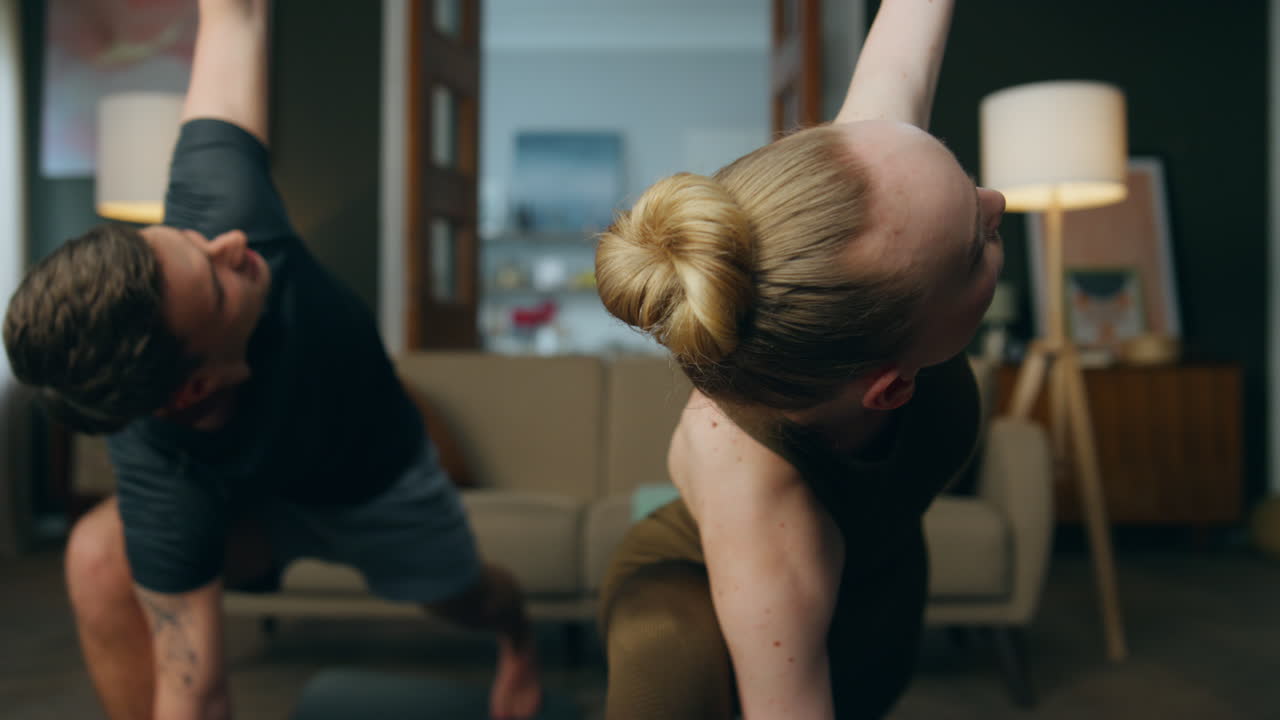 Zdatní partneři cvičí jógovou ásanu v místnosti zblízka. Pár cvičí společně.