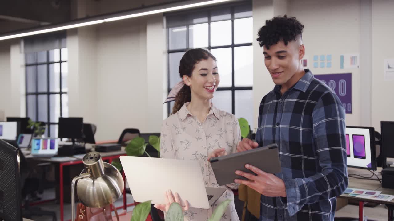 dos diseñadores creativos felices y diversos en discusión en una tableta en una oficina casual, cámara lenta