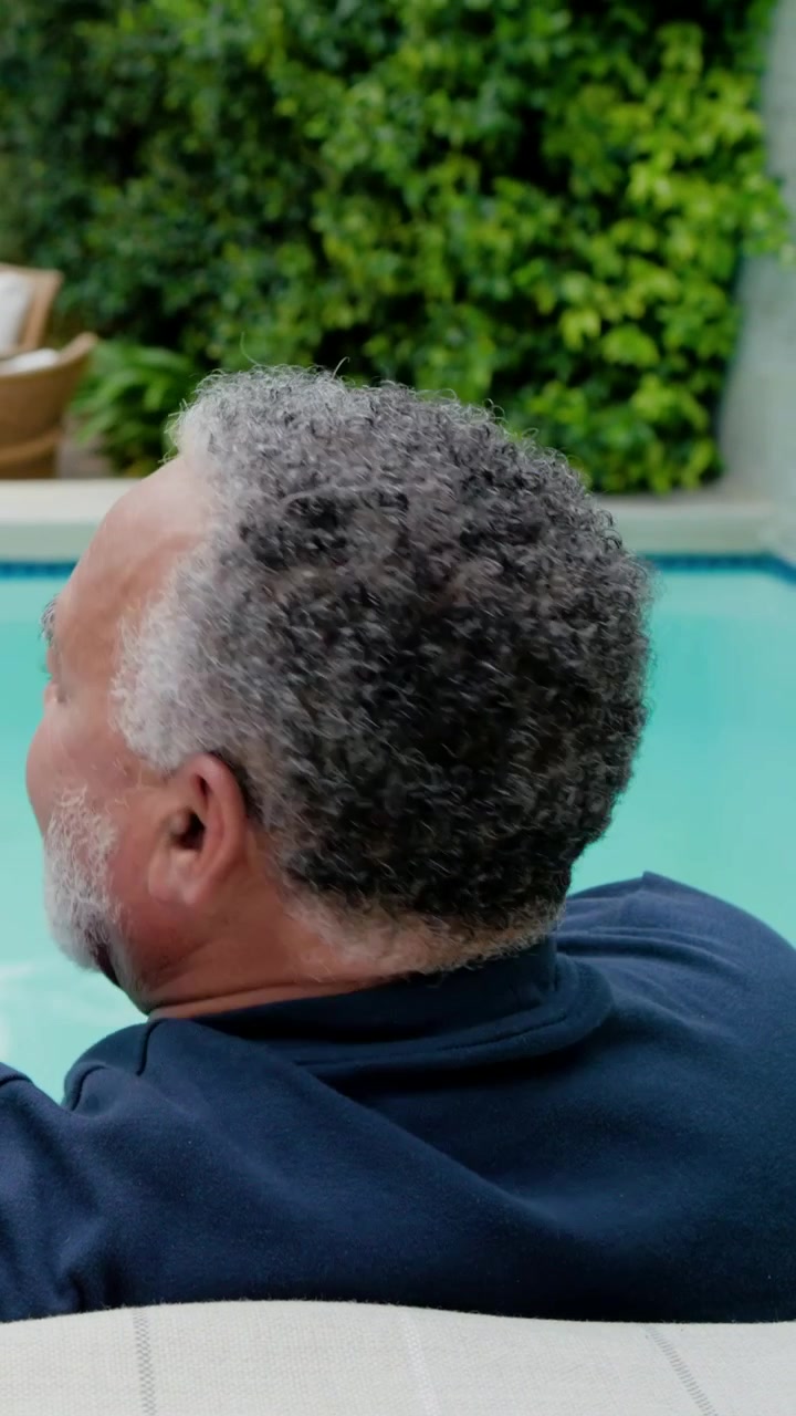 Vertical video: Turning man rotating head as camera starts at home pool, checking hedge, navy top