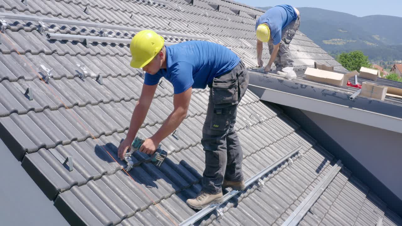 Two Adult Male Solar Installers Standing On Roof With Power Tools. Aerial View