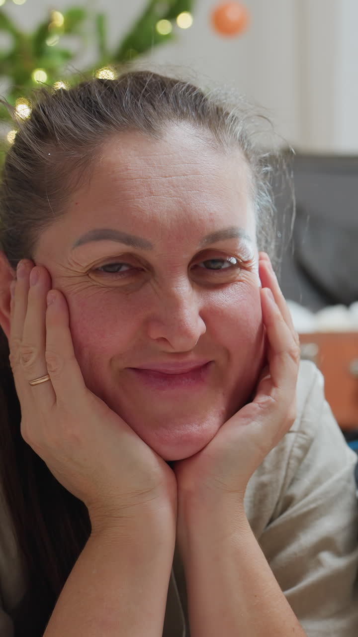 caucasian woman smiling near Christmas tree, bright eyes and hands cupping face, twinkling lights and kitchen background, playful laughter and joyful closeups, hostess prepping holiday treats