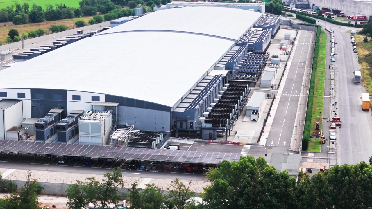 Vista dall'alto di un grande e moderno complesso di data center a Milano, con sistemi di raffreddamento, generatori e un parcheggio con pannelli solari