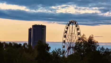 a ferris wheel and modern high-rises stand silhouetted against a golden sunset sky - medium shot