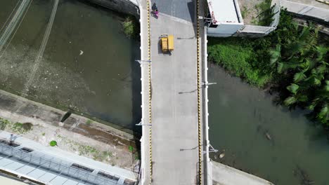 Aerial-top-down-view-along-street-with-mopeds-driving-over-bridge-in-tropical-town