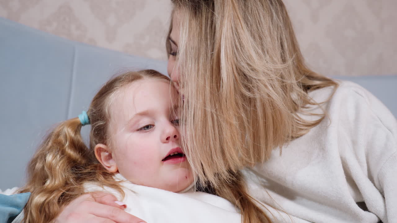 Mother sitting with daughter on bed, watching child talk while listening attentively, showing parental care, warmth, love, closeness, and bonding during family time in cozy home atmosphere of trust
