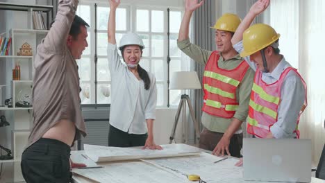 three asian engineers with helmets and a man celebrating finish drawing building construction while working at the office