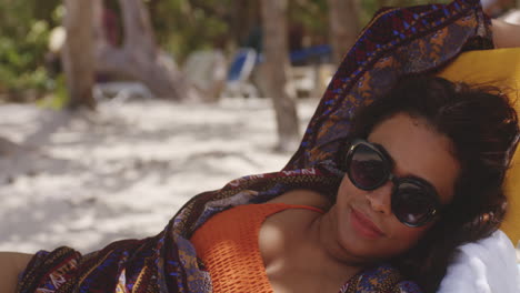 latin brunette lady relaxing on sun lounger in the shade enjoying beach holiday, medium shot