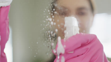 happy caucasian woman wearing rubber gloves and cleaning mirror at home