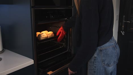 female model taking hot rolls out of a fan assisted oven with light on walking out of frame camera right