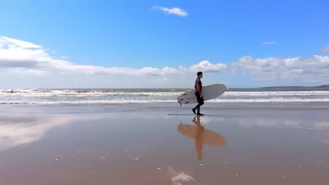 Männlicher-Surfer,-Der-An-Einem-Sonnigen-Tag-Mit-Surfbrett-Am-Strand-Spaziert-4k