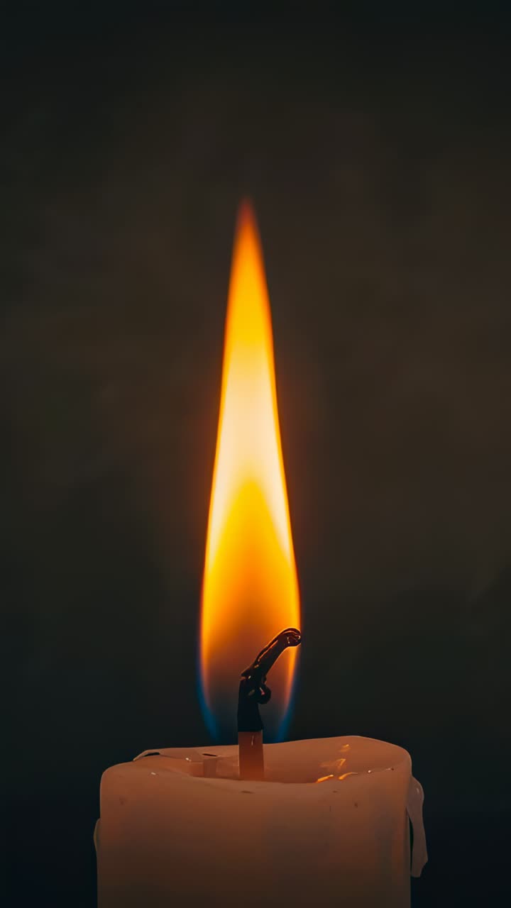 Video verticale: candela bianca tremolante che scioglie la cera, stoppino bruciato acceso che illumina una stanza buia