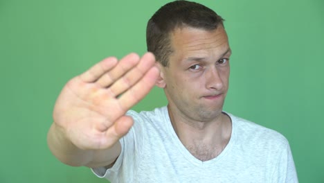 attractive man standing against chroma key saying no and making stop gesture with hand. green screen.