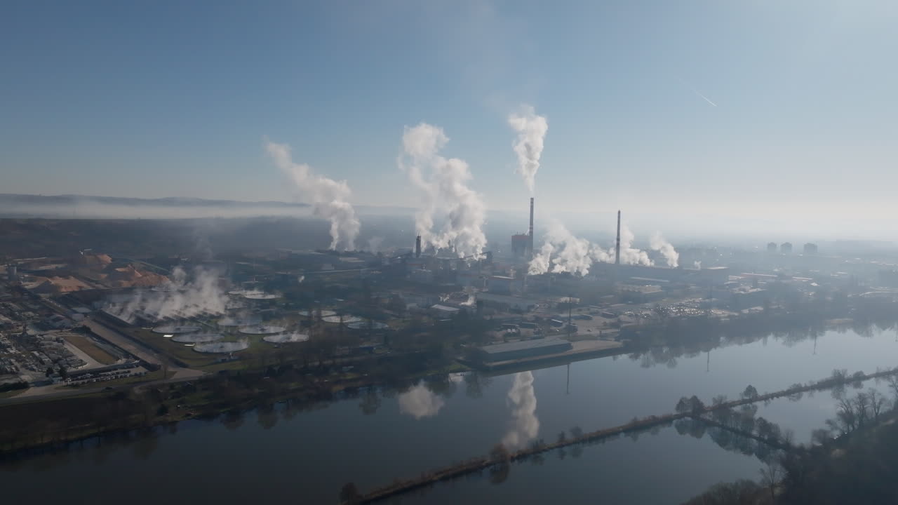 Toma de dron que muestra el complejo industrial de Štětí junto al río, con chimeneas expulsando vapor y reflejos visibles en la tranquila superficie del agua.