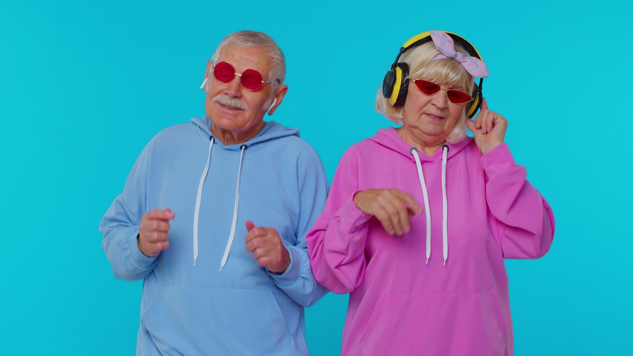 Senior stylish grandparents pensioners listening music via headphones, dancing disco fooling around