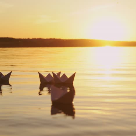 several white paper boats on water at sunset. paper ships in water. origami.
