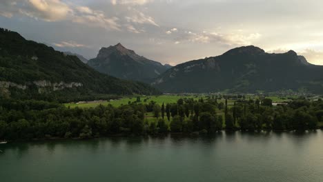 Herrliche-Aussicht-Auf-Die-Berge-Während-Eines-Sonnenuntergangs,-Der-Lichter-Durch-Die-Wolken-Wirft,-Himmlische-Offenbarungen,-Fließender-Fluss,-Viele-Bäume-Und-Eine-Kleine-Stadt-Am-Fuße-Des-Rechten-Berges,-Gefühl-Der-Ruhe