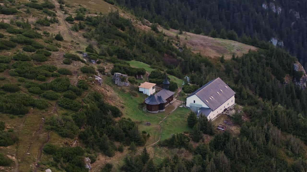 Small monastery in the mountains, surrounded coniferous green trees by aerial close up view