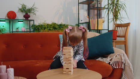 funny little one teen kid girl play wooden tower blocks bricks game at home in modern living room