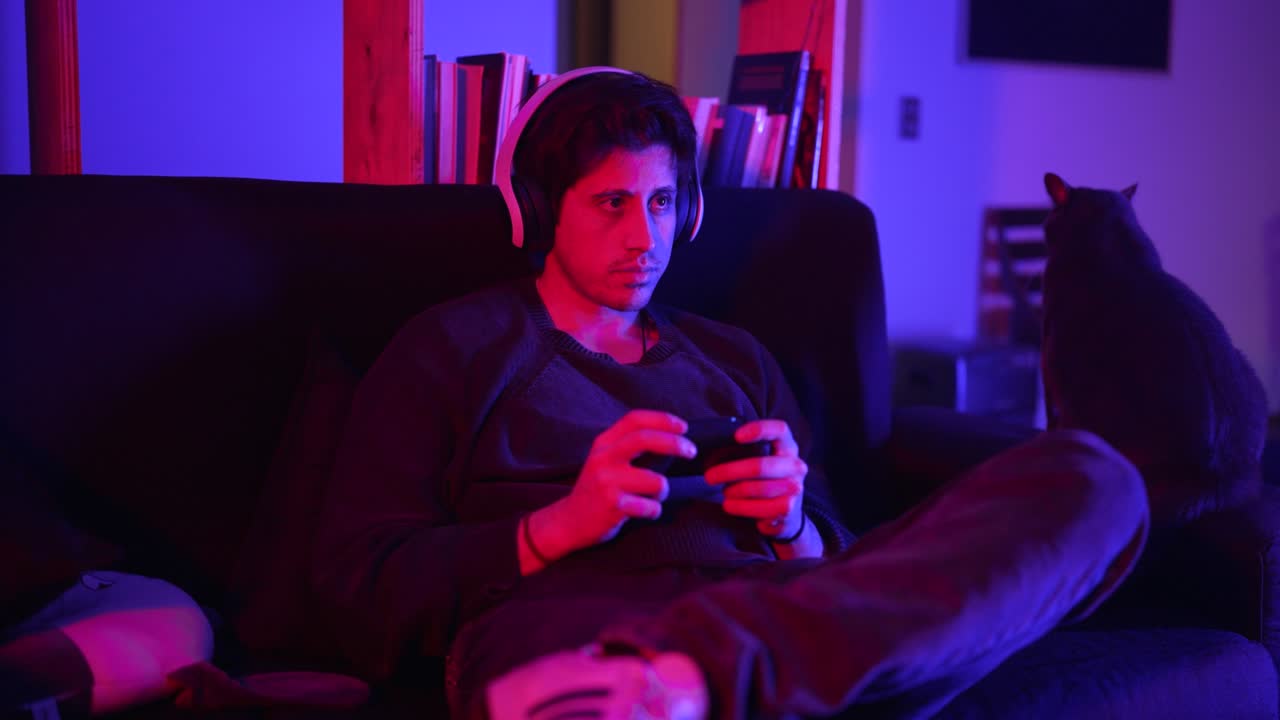 a man with a more serious tone in a medium shot plays video games in his apartment