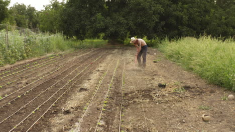 farmer using a rake farming tool to till the land and soil during a hot day