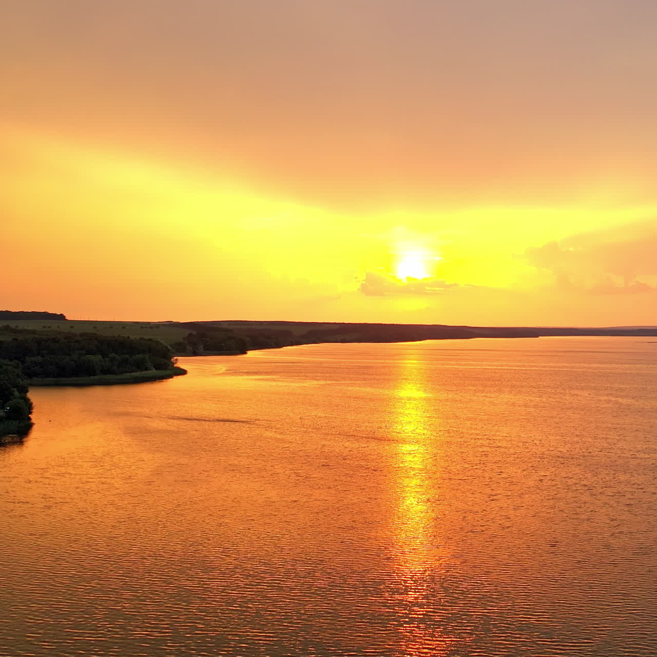 Beautiful orange sunset over the calm river. Natural landscape of green forest and river in the evening. Aerial view. Camera moves left.