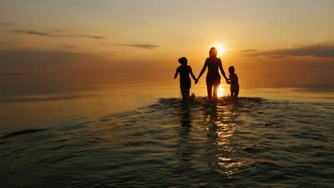Mutter-Mit-Zwei-Kindern-Geht-Bei-Sonnenuntergang-Lachend-Im-Meer-Schwimmen