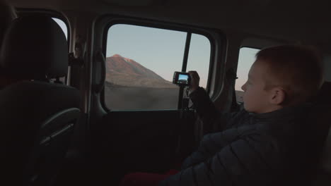 a boy on the backseat of the driving car shooting the mountain landscape