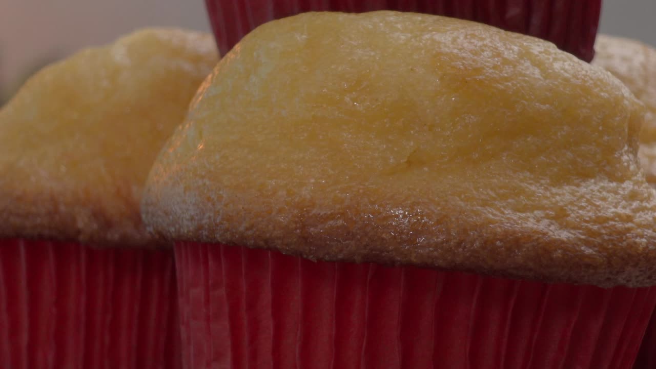 Tamales cupcakes nestled in vibrant red paper cups create an enticing display of baked goods, featuring a soft texture and a delightful dusting of powdered sugar, perfect for any celebration