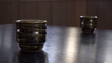 pan up over two japanese cups on a table inside a restaurant setting with outside window reflections on surface