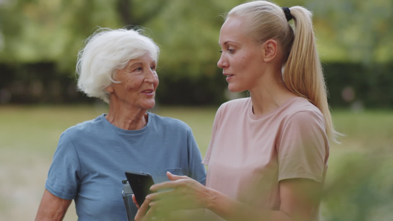 Istruttrice e donna anziana che conversano e usano lo smartphone all'aperto