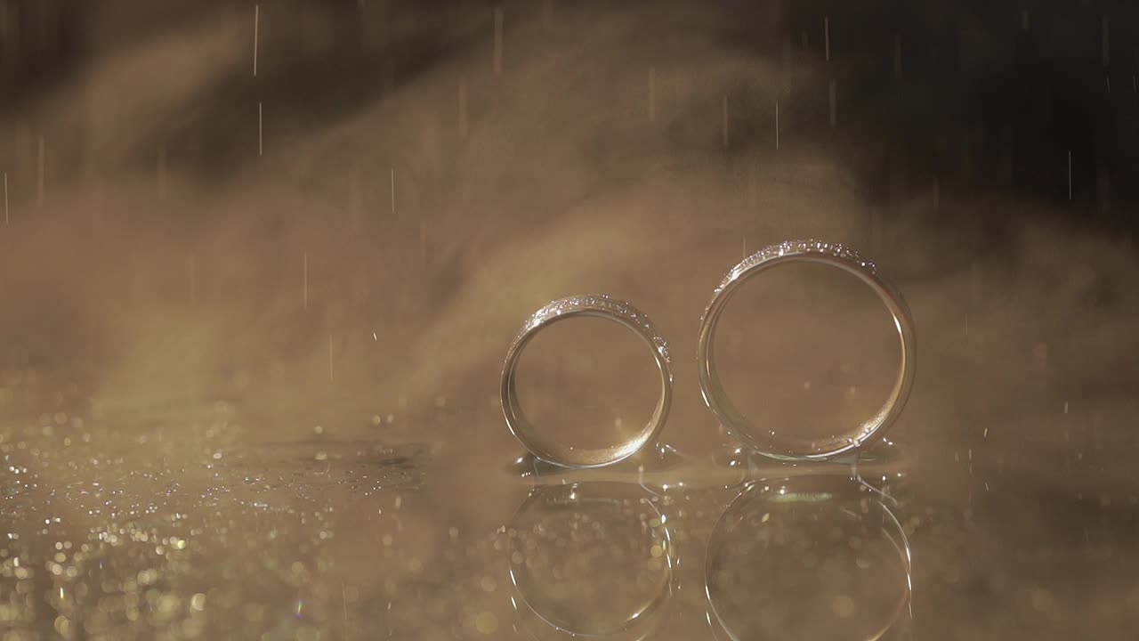 Wedding rings on dark water surface shining with light. Water drops. Close up