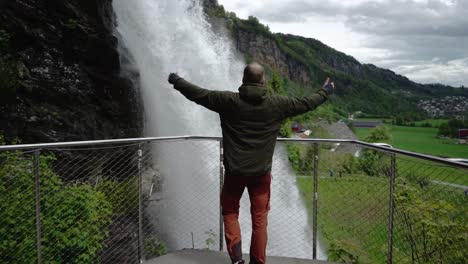 Toma-En-Cámara-Lenta-Del-Hombre-Levantando-Los-Brazos-Frente-A-La-Gigantesca-Cascada-En-Noruega---Cámara-Lenta