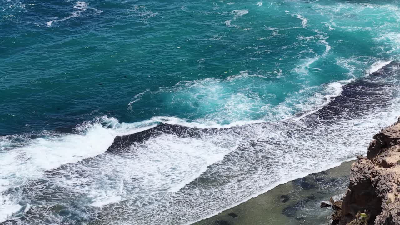 Riprese aeree dall'alto con drone catturano onde turchesi che si infrangono su rocce frastagliate e piscine costiere naturali