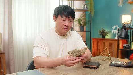 asian man frowning at nearly empty wallet sees only coins slowly shakes head with mild discontent
